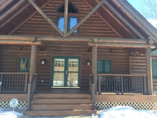 Log house with wood deck, brown banisters, and green trim door